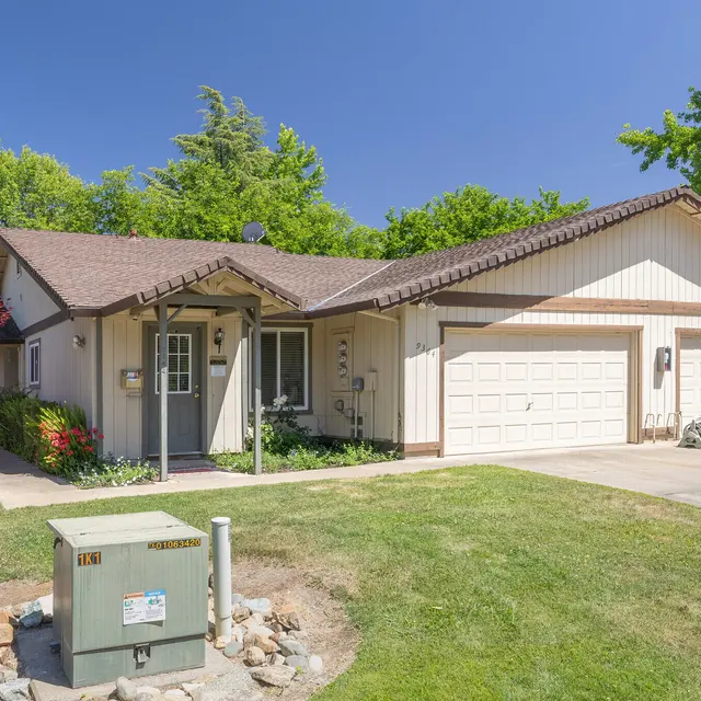 A single-story house with a porch and two garages surrounded by greenery and a sign that reads 'Leasing Office.'