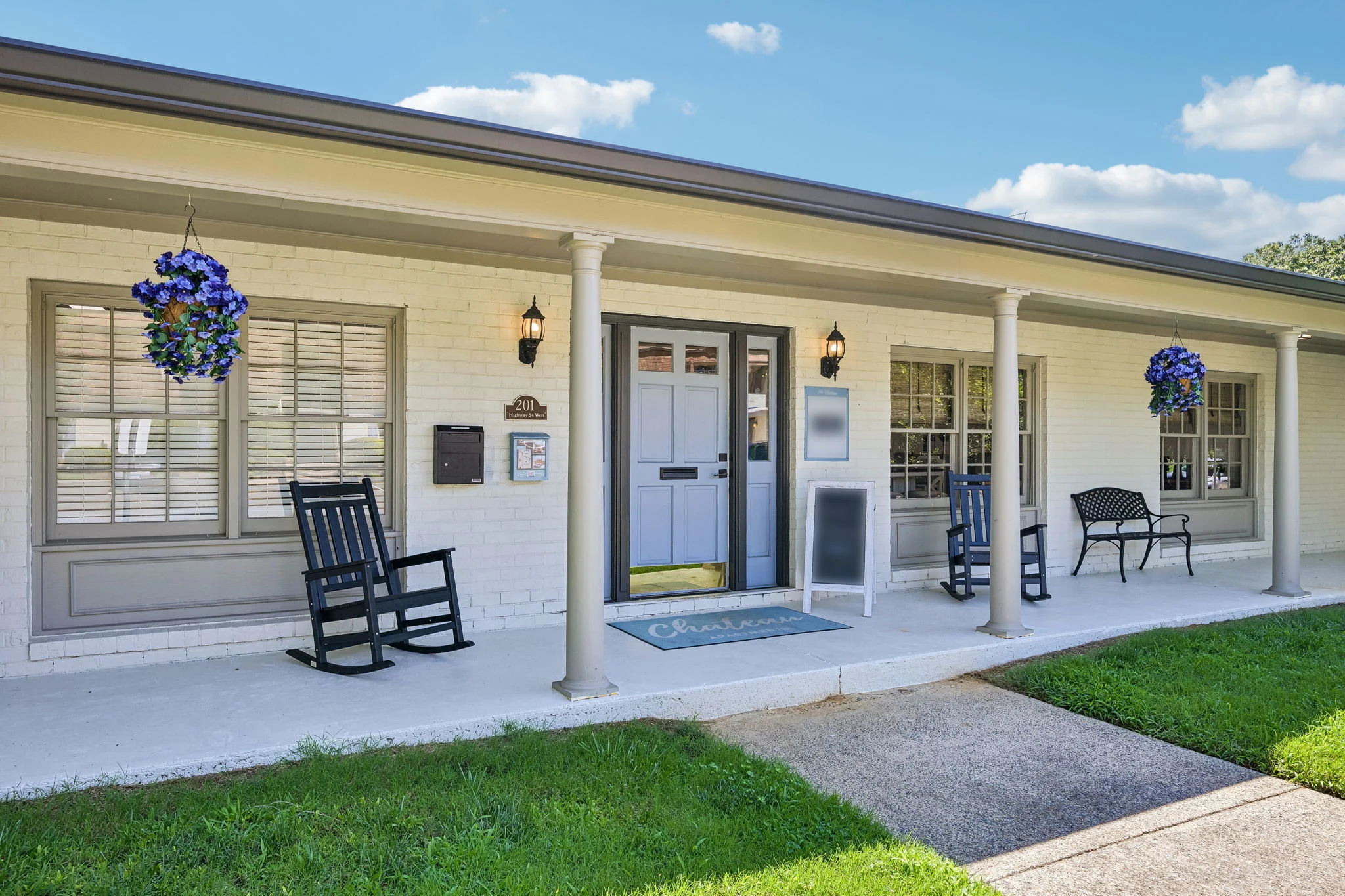 Exterior view of a welcoming apartment community entrance with rocking chairs and floral decorations.