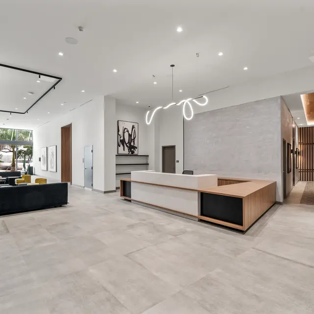A spacious and modern lobby with a reception desk, seating area, and contemporary decor. Large windows allow natural light to fill the room, showcasing the minimalist design with neutral colors and stylish furniture.