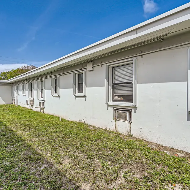 A view of the side of a low-rise building, showing a grass area and several windows.
