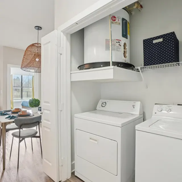 A laundry area with a washer and dryer in an open-concept space, featuring a table for dining or work in the background.