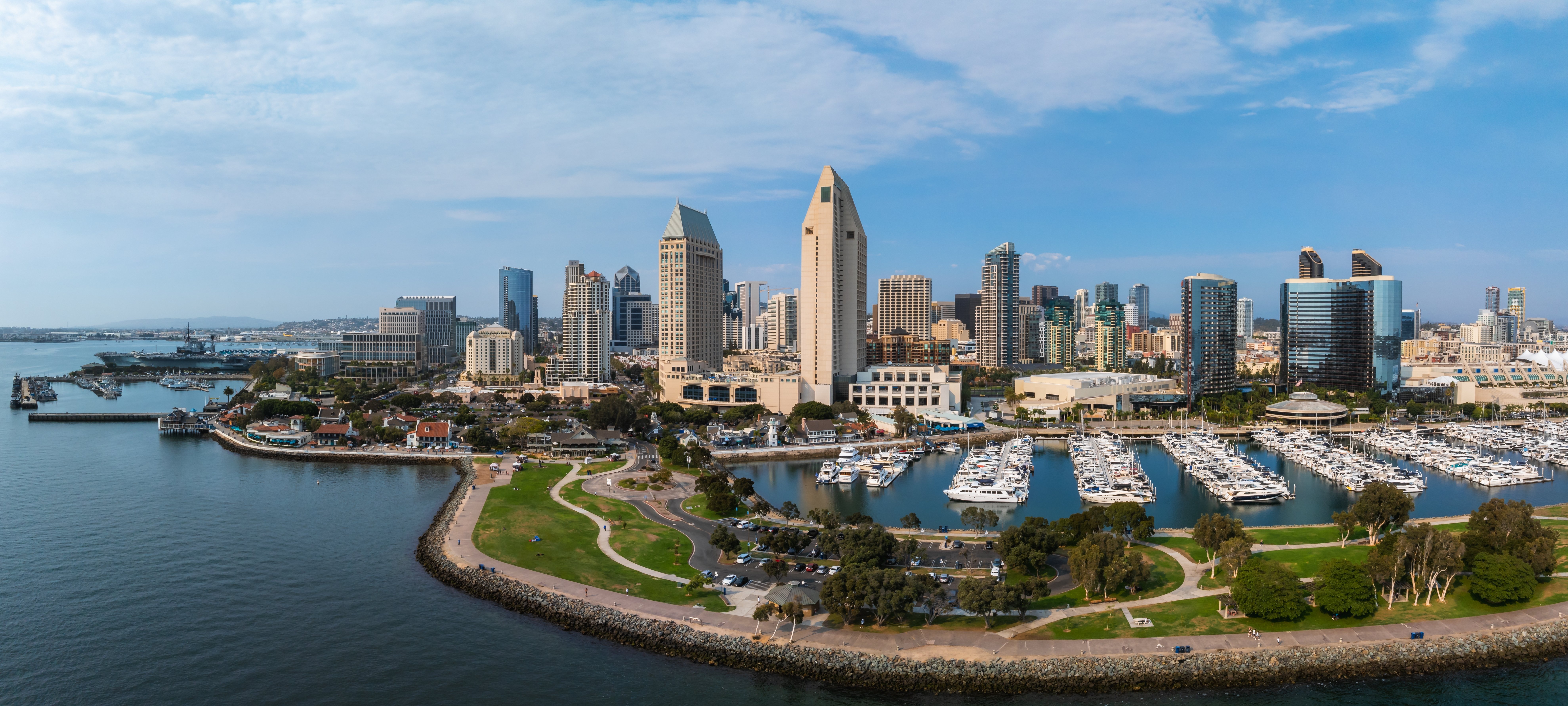 A panoramic view of San Diego's skyline featuring tall buildings and a marina filled with boats, along with a blue sky and water in the foreground.