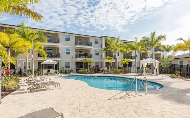 Residential Pool Area A sunny residential pool area with palm trees, lounge chairs, and an adjacent building.