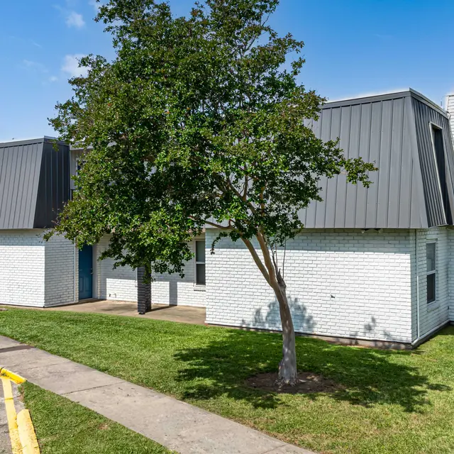 A modern townhouse complex featuring several units with distinct slanted roofs and white brick exteriors, surrounded by green grass and a tree.