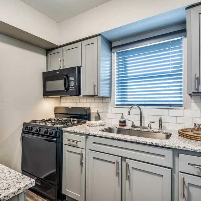 A modern kitchen featuring gray cabinets, stainless steel appliances, and a granite countertop.
