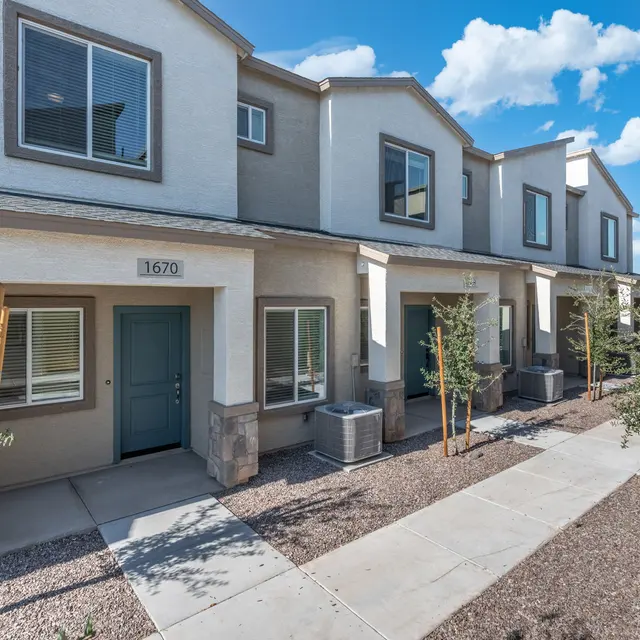Contemporary Townhouses Modern townhouses with beige stucco walls and green doors, featuring a pathway and decorative plants.