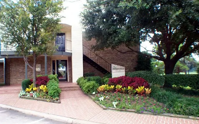 A brick building with a staircase leading to the upper level, surrounded by well-maintained greenery and colorful flower beds.