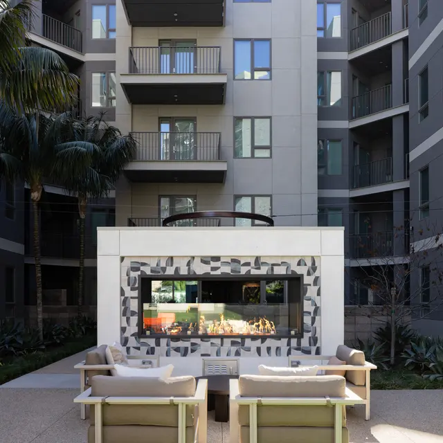 A modern courtyard in an apartment complex featuring seating, a wall-mounted artwork, and tropical plants.