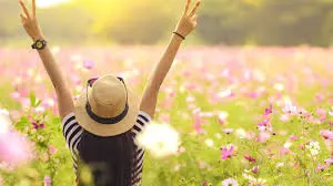 Woman Celebrating in a Flower Field A woman wearing a hat and stripped shirt standing in a field of flowers, raising her arms in a victorious pose.