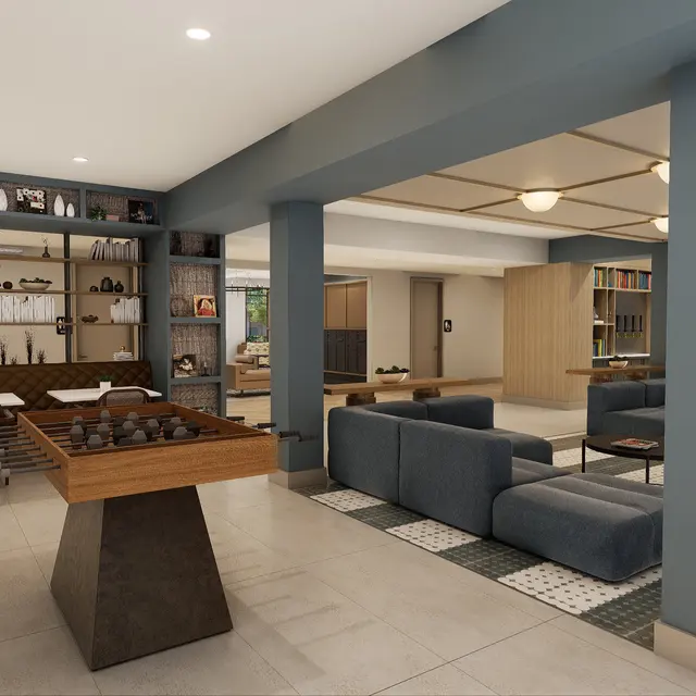 A modern and spacious living area featuring a seating arrangement with dark blue couches and a decorative table. There are bookshelves and art displayed on walls, along with a dining area in the background.