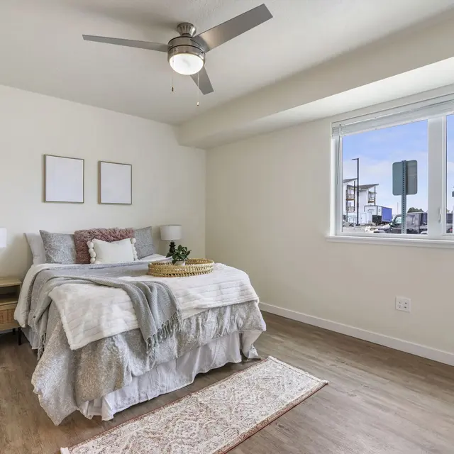 Modern Bedroom Interior A modern bedroom featuring a queen bed with light bedding, a decorative throw blanket, and a stylish rug. There are two lamps on either side of the bed, and large window revealing a view of the outdoors.