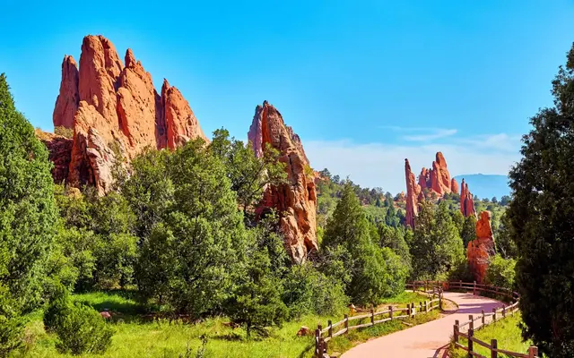 A scenic view of red rock formations surrounded by lush green trees and a winding path.
