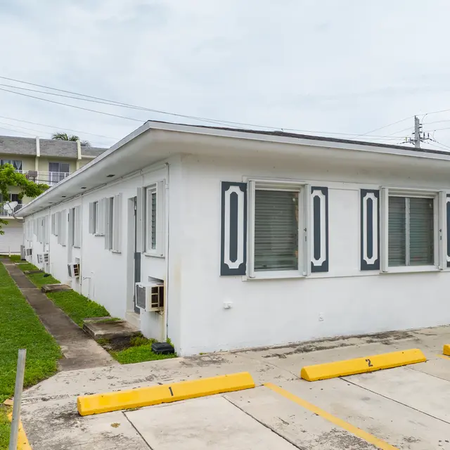 Exterior view of a white apartment complex with several units, grassy area, and parking spots.