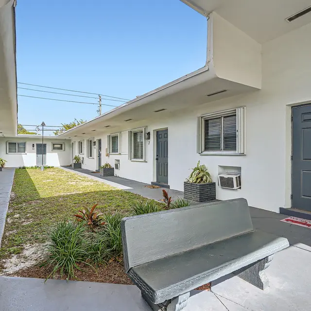 A view of a motel's courtyard featuring several doors to rooms, a grassy area, and potted plants.