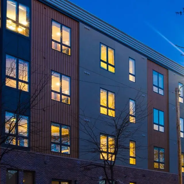 Exterior view of Woodrow Apartments in Fargo, ND at night, featuring large illuminated windows and modern urban architecture.