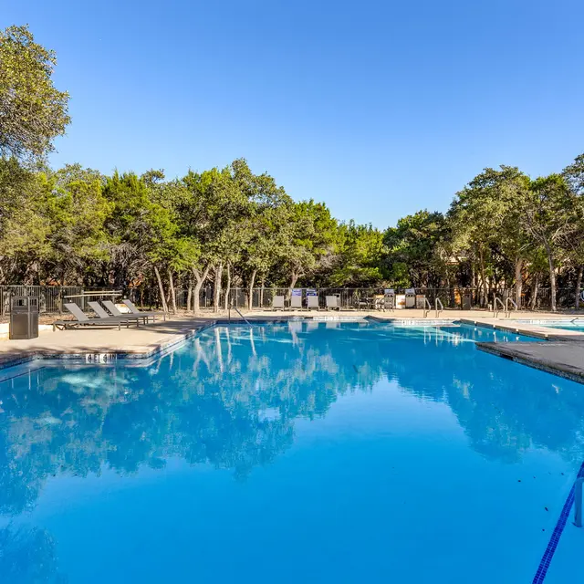 A serene swimming pool surrounded by trees and clear blue sky.