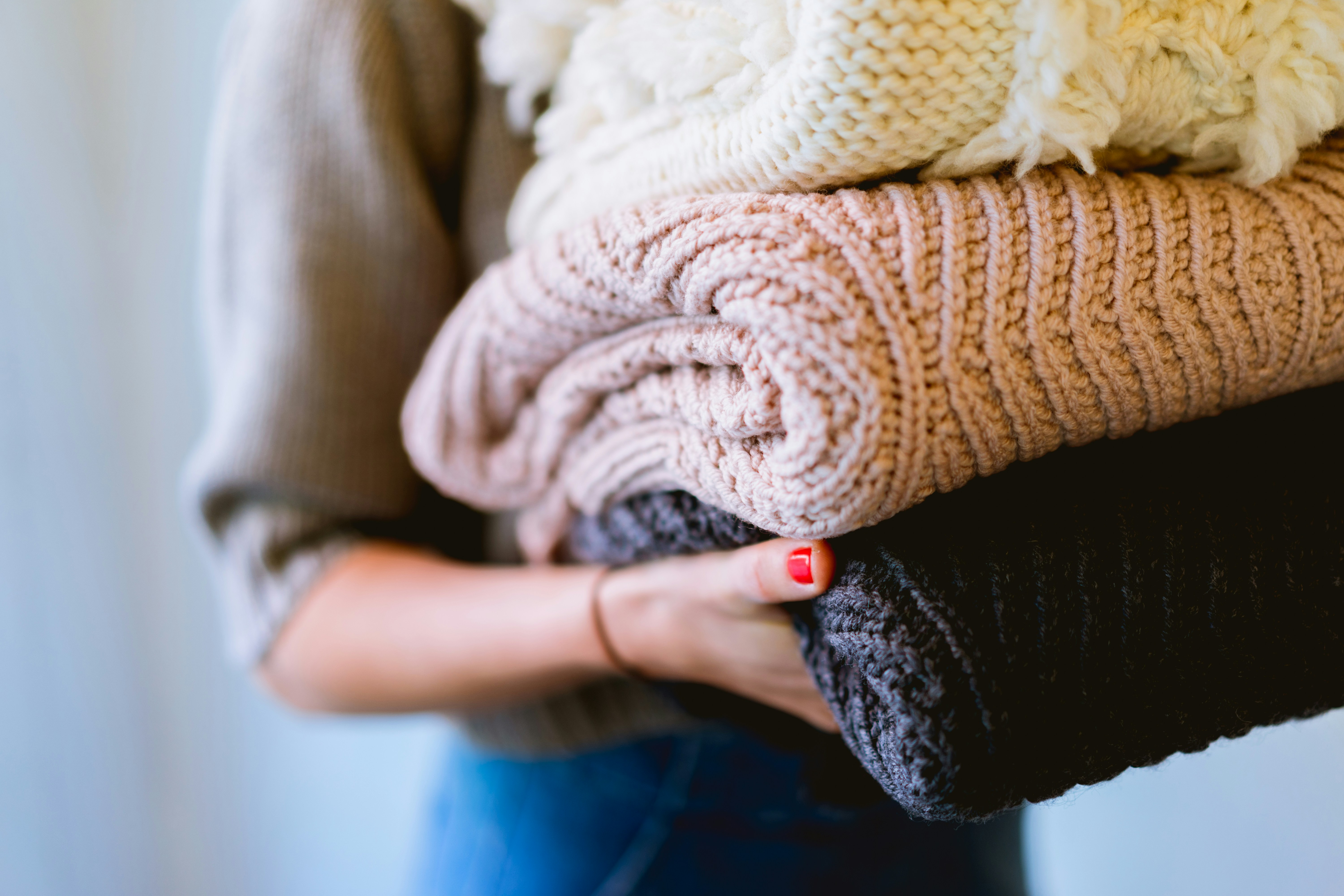 Cozy Blankets for Warmth A person holding three neatly folded blankets in varying colors of cream, beige, and dark gray, with their hand visible near the bottom.