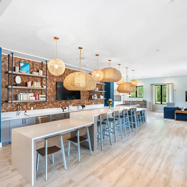 Modern Kitchen and Living Area A spacious modern kitchen and living area with a large island, silver bar stools, and hanging pendant lights. The kitchen features a contemporary design with a wooden accent wall and open shelving. There are windows that allow natural light to fill the space, and stylish furnishings in the living area including a blue couch and wooden dining table.