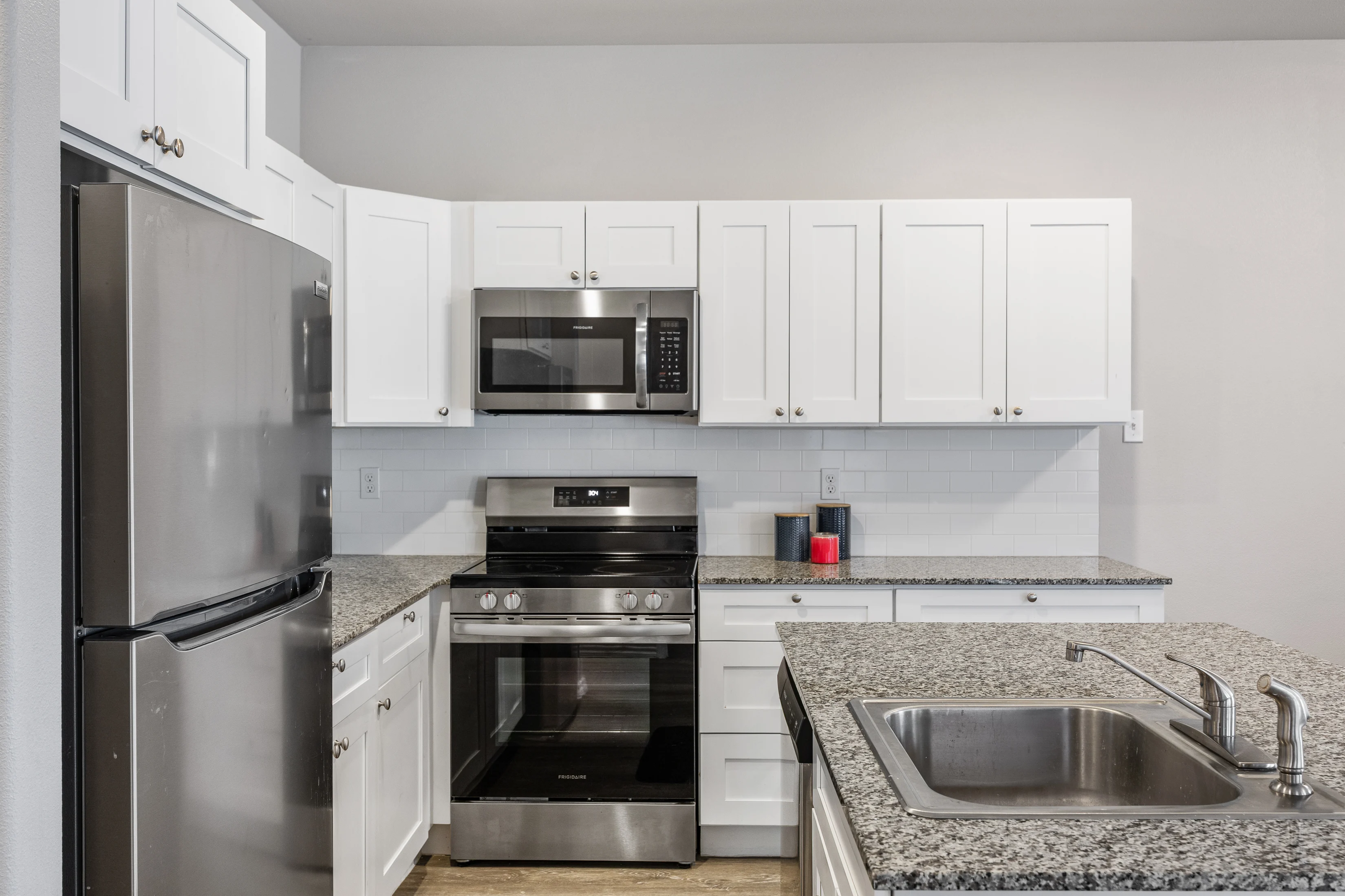 Modern kitchen featuring stainless steel appliances, white cabinetry, and a granite countertop.