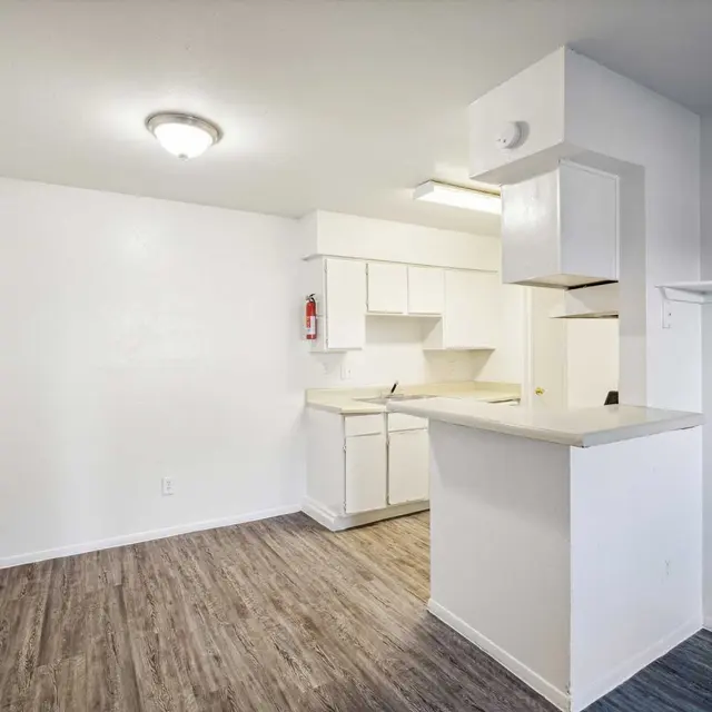 A modern kitchen space with light-colored walls, wooden flooring, and white cabinetry.