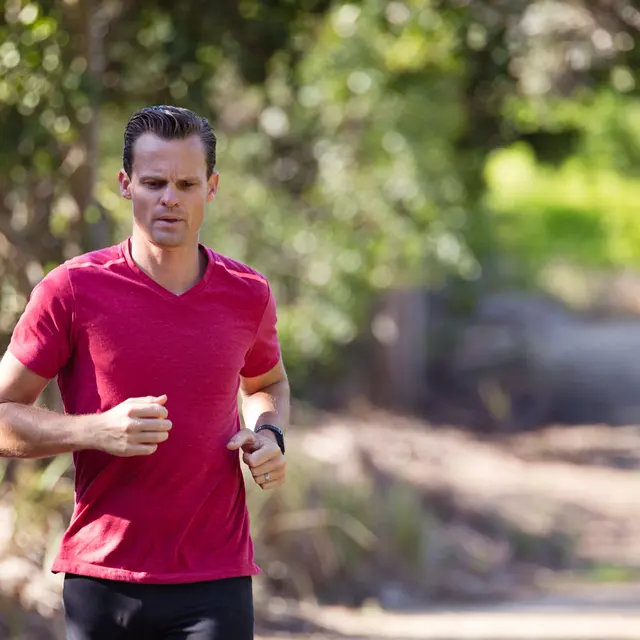 A man running on a dirt path surrounded by greenery.