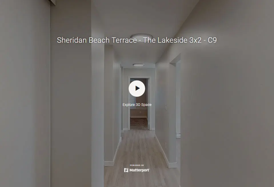 A well-lit hallway in a residential setting with light-colored walls and flooring, featuring a visible doorway at the end and soft ceiling lights.