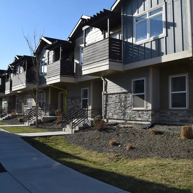 Modern Townhouses in a Suburban Setting A row of modern townhouses featuring stone and wood facades, front balconies, and landscaped pathways.