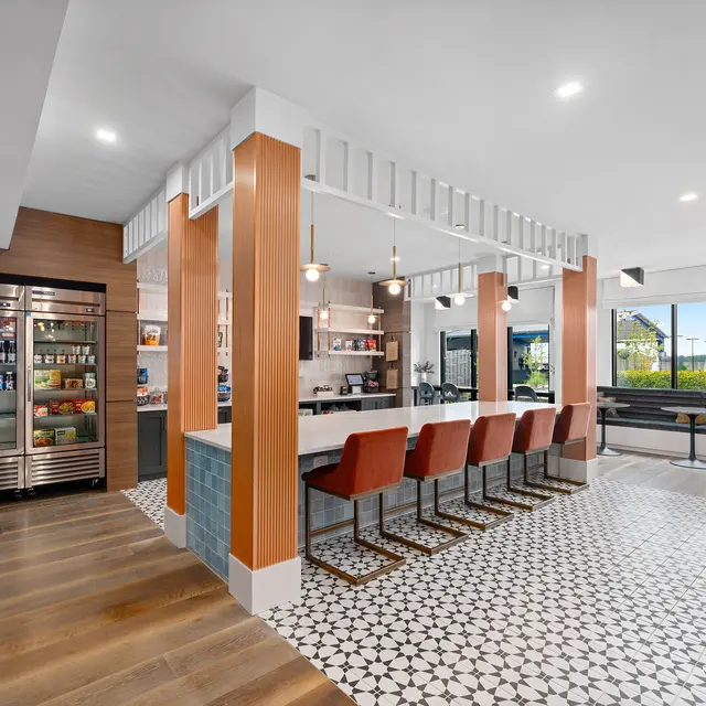 A modern kitchen space with a large island and seating, featuring a subtle patterned floor, a beverage refrigerator, and large windows letting in natural light.