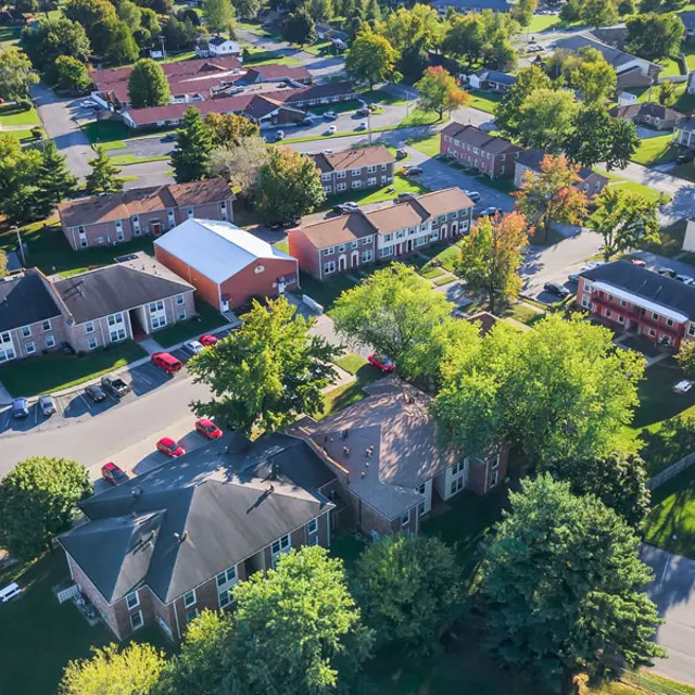 Aerial view of a residential neighborhood with various buildings, green trees, and parked cars.
