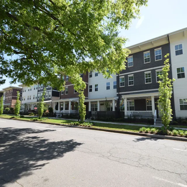 A row of modern apartment buildings on a sunny day, lined with young trees along the street.