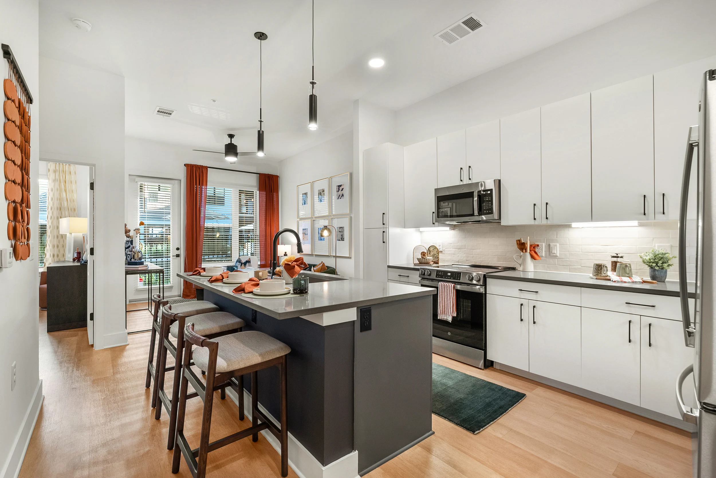 A modern kitchen featuring a central island with bar stools, contemporary cabinetry, and stainless steel appliances. Large windows let in natural light, and decorative items are placed on the counter.