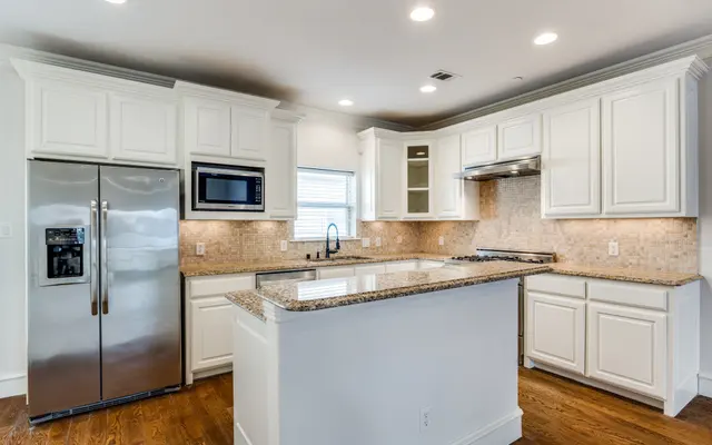 Modern Kitchen Design Bright and spacious kitchen featuring white cabinets, granite countertops, and stainless steel appliances including a refrigerator and microwave.