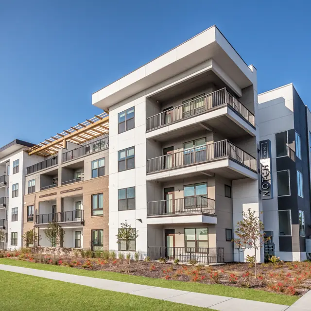 A modern apartment building with multiple balconies and a landscaped garden in front.