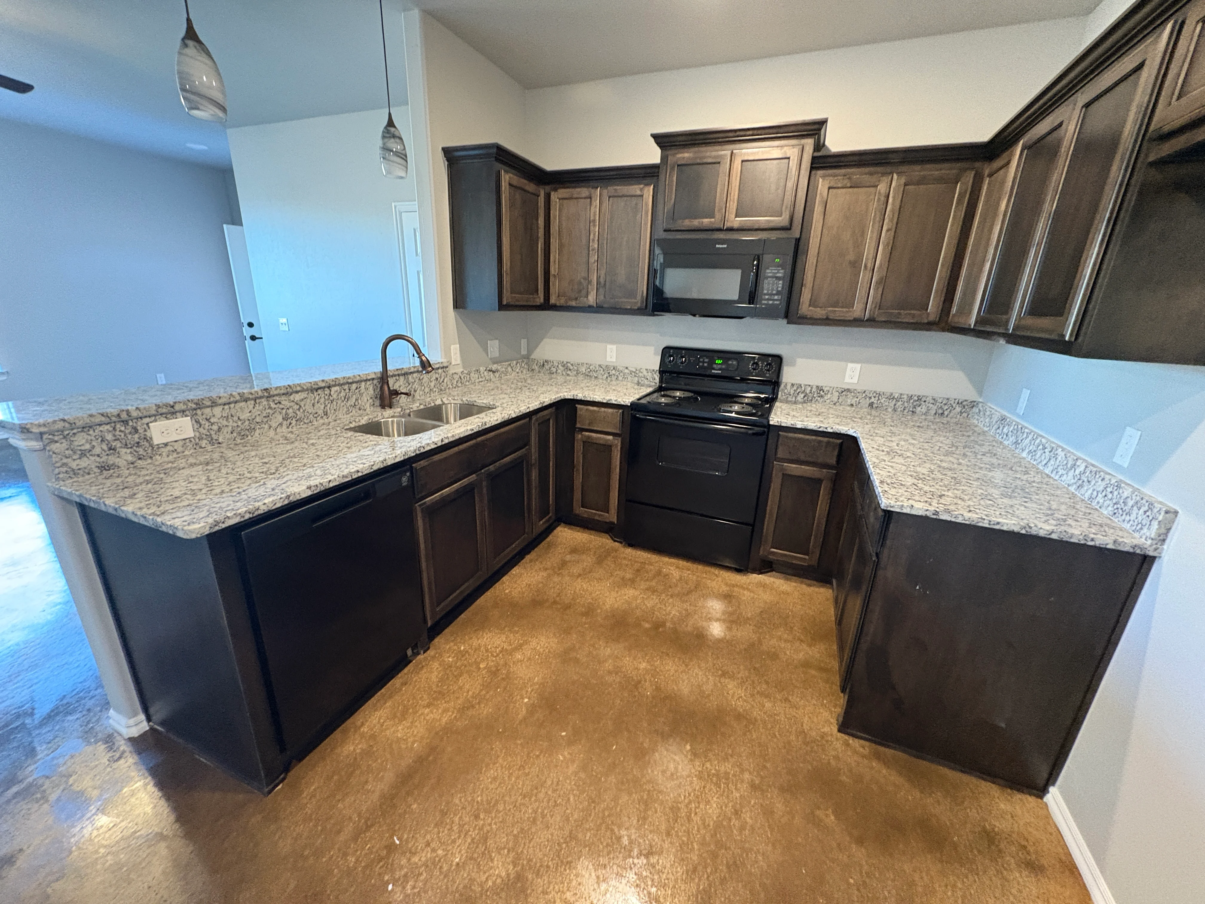 Modern Kitchen Design A modern kitchen featuring dark wood cabinetry, granite countertops, and stainless steel appliances. The floor has a polished concrete finish.