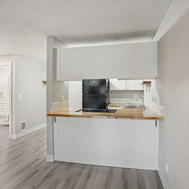 Modern Kitchen Area A modern kitchen area with a bar countertop, featuring a black refrigerator and white cabinetry, set on a light wooden floor.