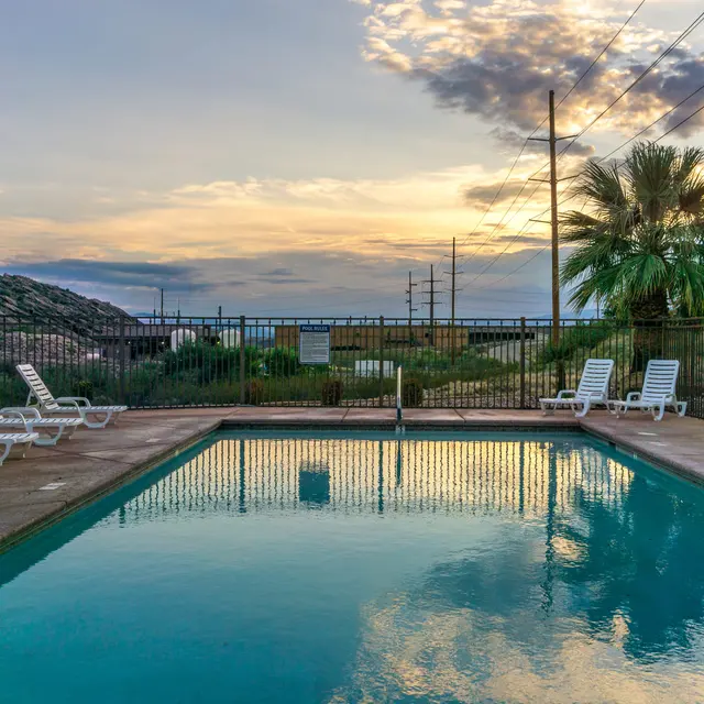 A serene swimming pool at sunset, surrounded by lounge chairs and lush greenery, with rolling hills in the background.