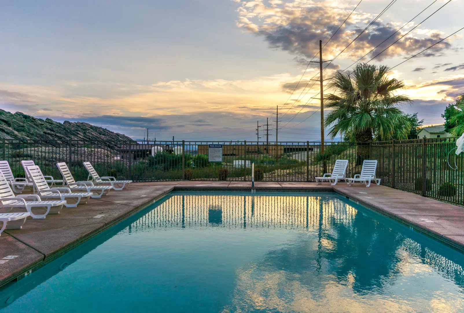 A serene swimming pool at sunset, surrounded by lounge chairs and lush greenery, with rolling hills in the background.