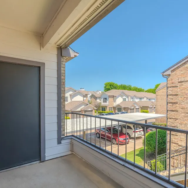 View from a balcony overlooking a parking area and neighboring buildings in an apartment complex.