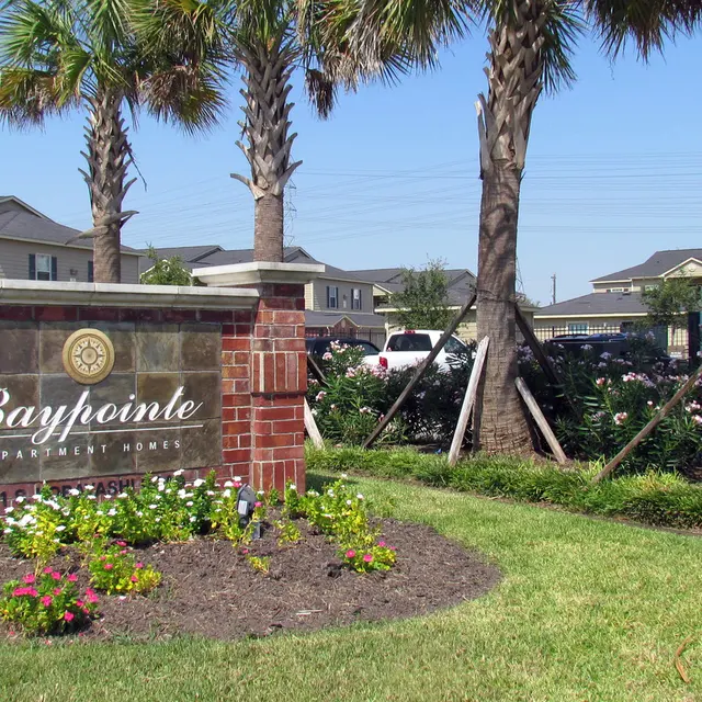 A landscaped sign for Baypointe, featuring flowers and palm trees, with residential buildings in the background on a sunny day.