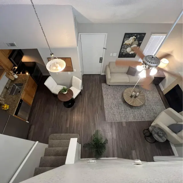 Aerial view of a modern living room with a kitchen, featuring a couch, chairs, coffee table, and a decorative rug.