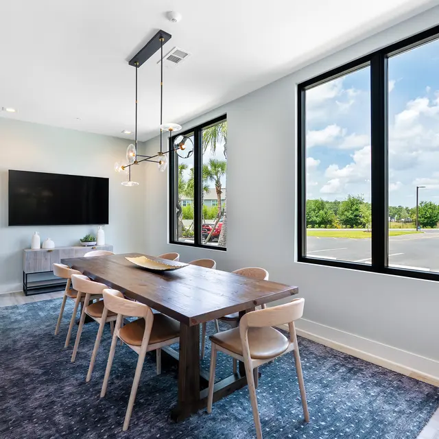 Stylish Dining Room Decor A modern dining room featuring a long wooden table with eight chairs, a large window providing natural light, and a wall-mounted television. The room has a light blue color scheme and a plush area rug.