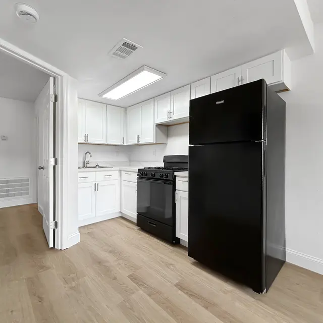 Modern Apartment Kitchen A modern kitchen featuring black appliances including a refrigerator and stove, white cabinetry, and hardwood flooring.