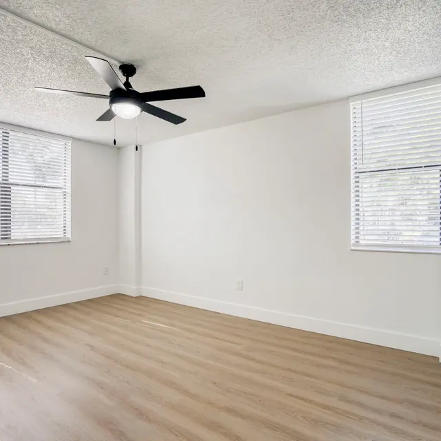 Empty Room with Ceiling Fan An empty room featuring a ceiling fan, hardwood-like flooring, and two windows with blinds.