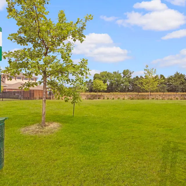 Park Cleanliness Reminder for Pet Owners A green sign instructing pet owners to keep the area clean, attached to a waste disposal station in a grassy park with a small tree.