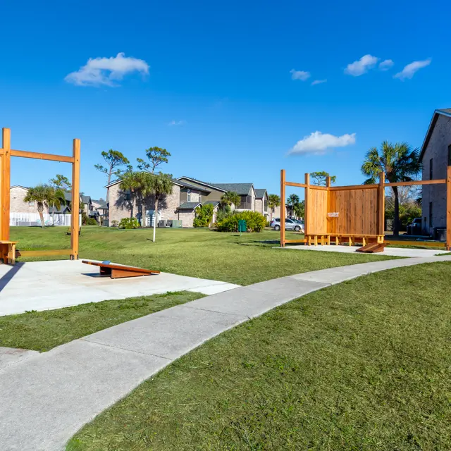 A sunny park featuring wooden exercise structures on a grassy area with palm trees in the background.