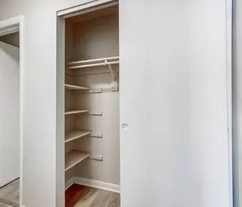 An empty closet with several shelves and a hanging rod, featuring a sliding door, set against a neutral wall.