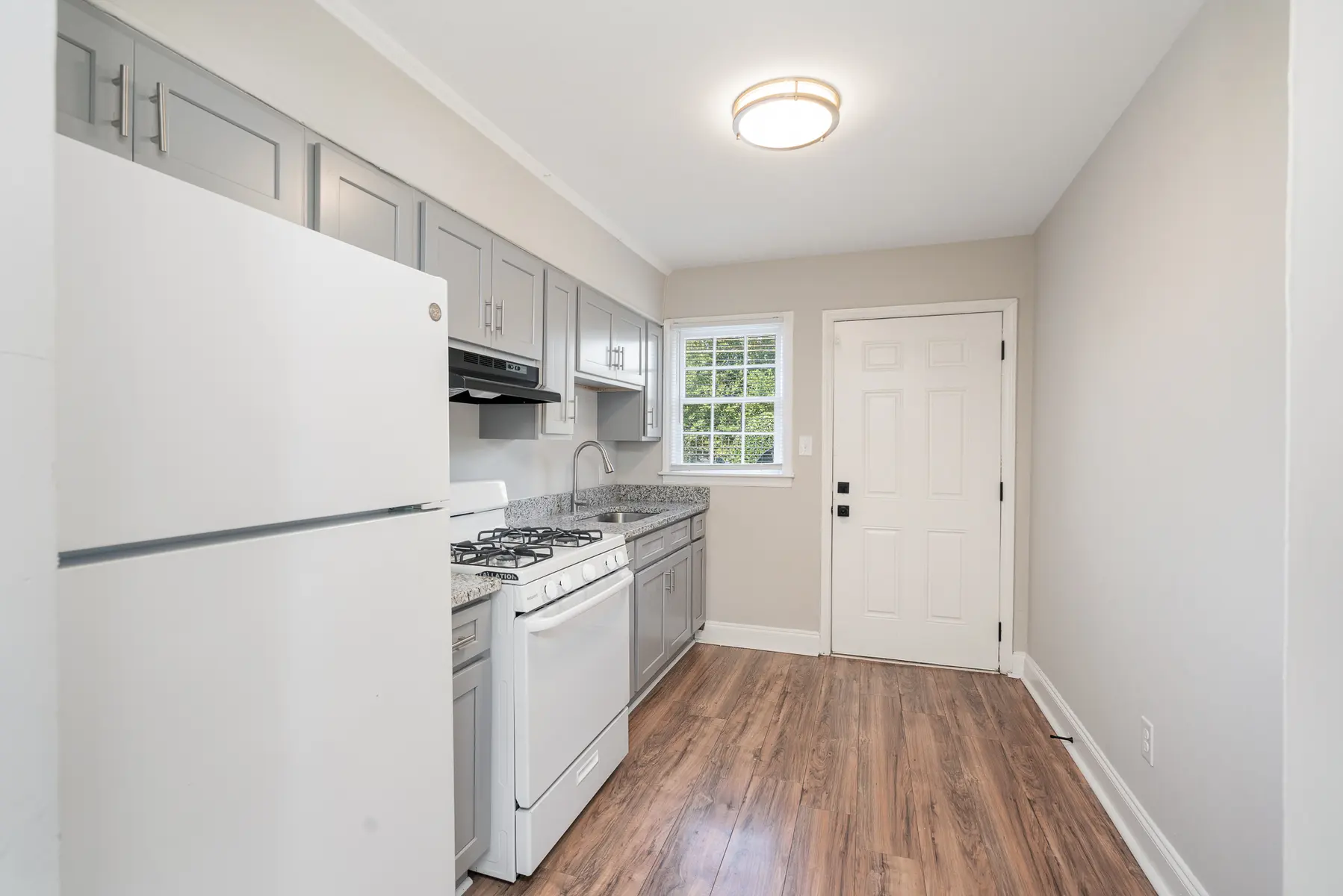 A modern kitchen featuring a white refrigerator, stainless steel oven, and grey cabinets with a window view.