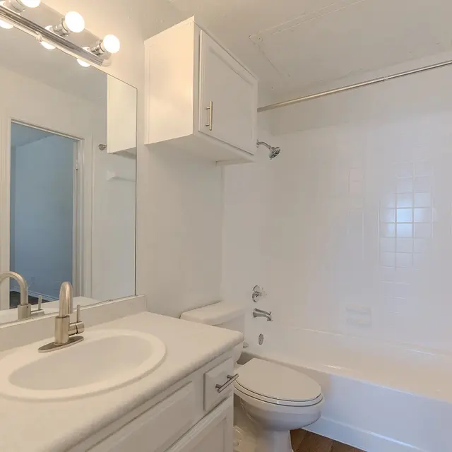A clean and modern bathroom with a white color scheme, featuring a sink with a mirror, a bathtub, and a toilet.