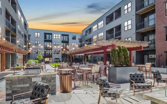 A modern apartment complex courtyard featuring seating arrangements, potted plants, and a sunset sky above.