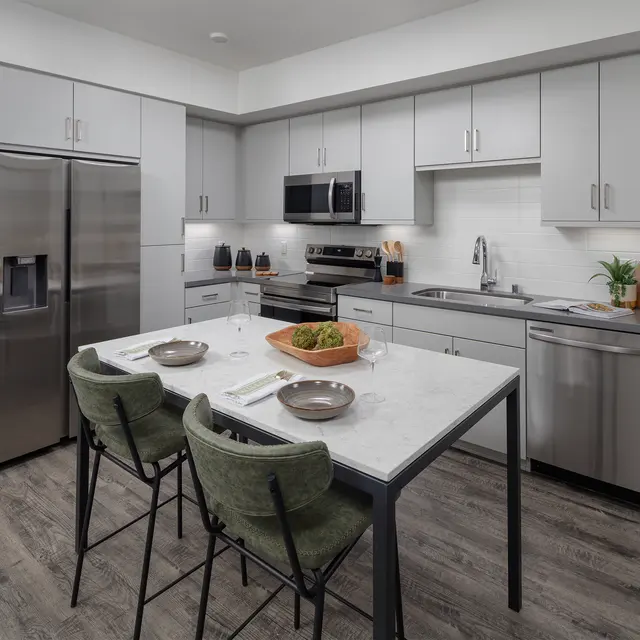 A modern kitchen with stainless steel appliances, grey cabinetry, and a white marble table set for dining.